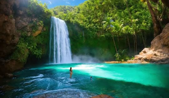 A person swimming in the water near a waterfall.